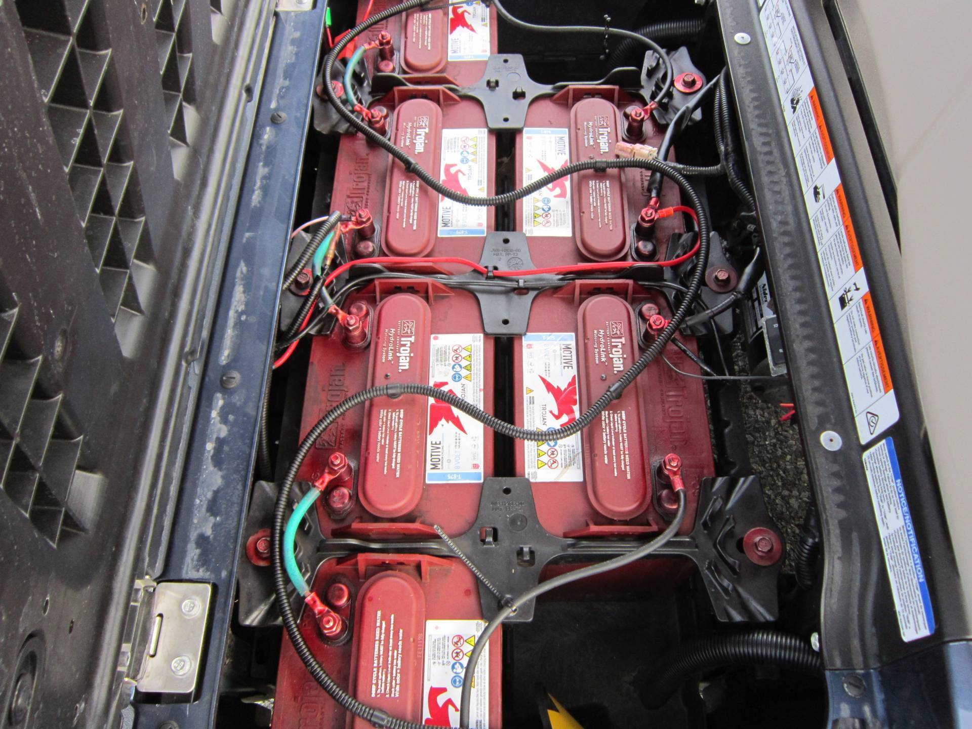 Close-up of six Trojan batteries connected with cables in the compartment of an electric vehicle, showcasing their labels and connections.